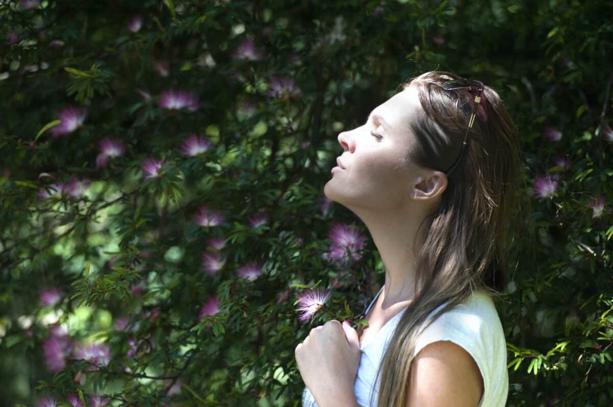 woman standing next to a tree with purple flowers breathing in the fresh air