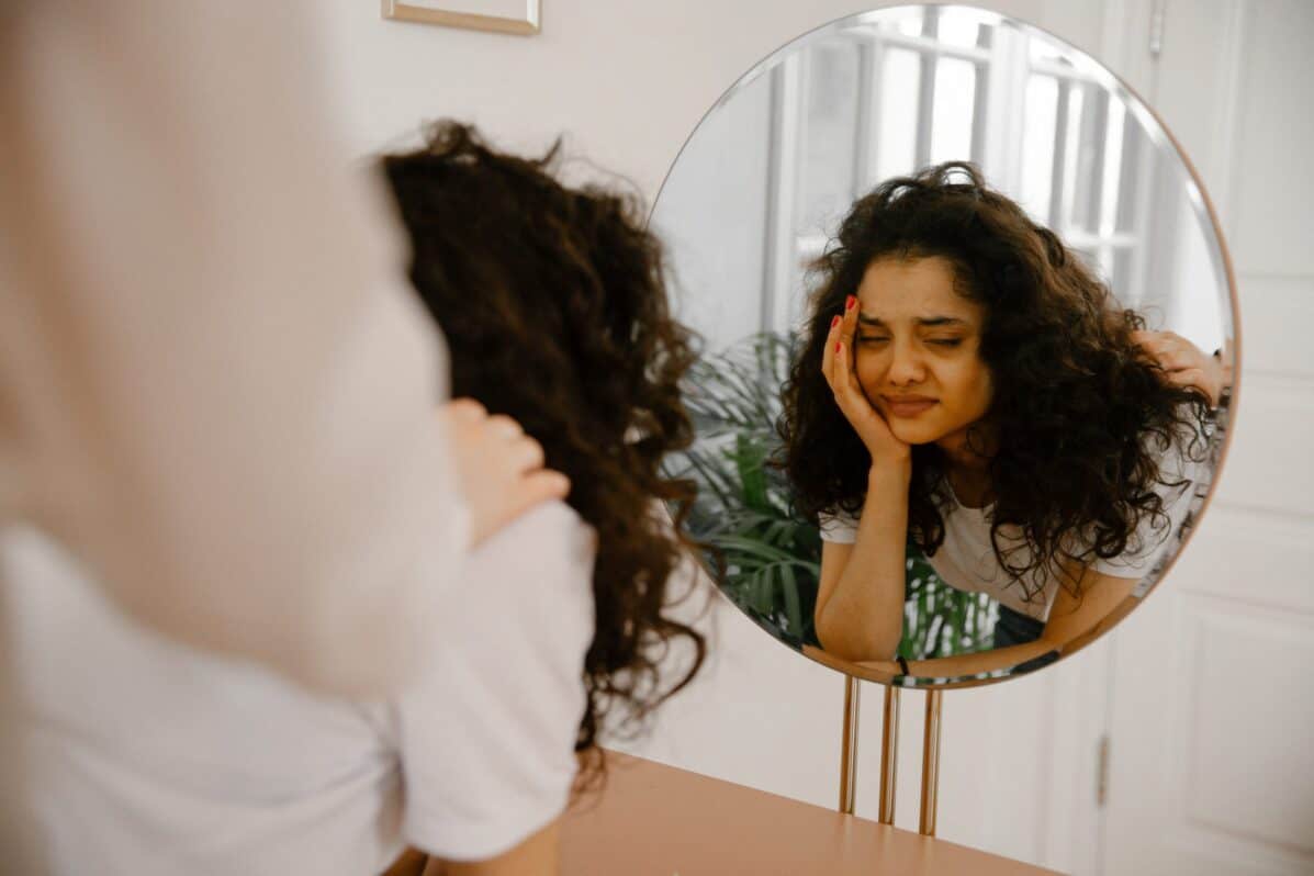 woman experiencing stress while looking in the mirror