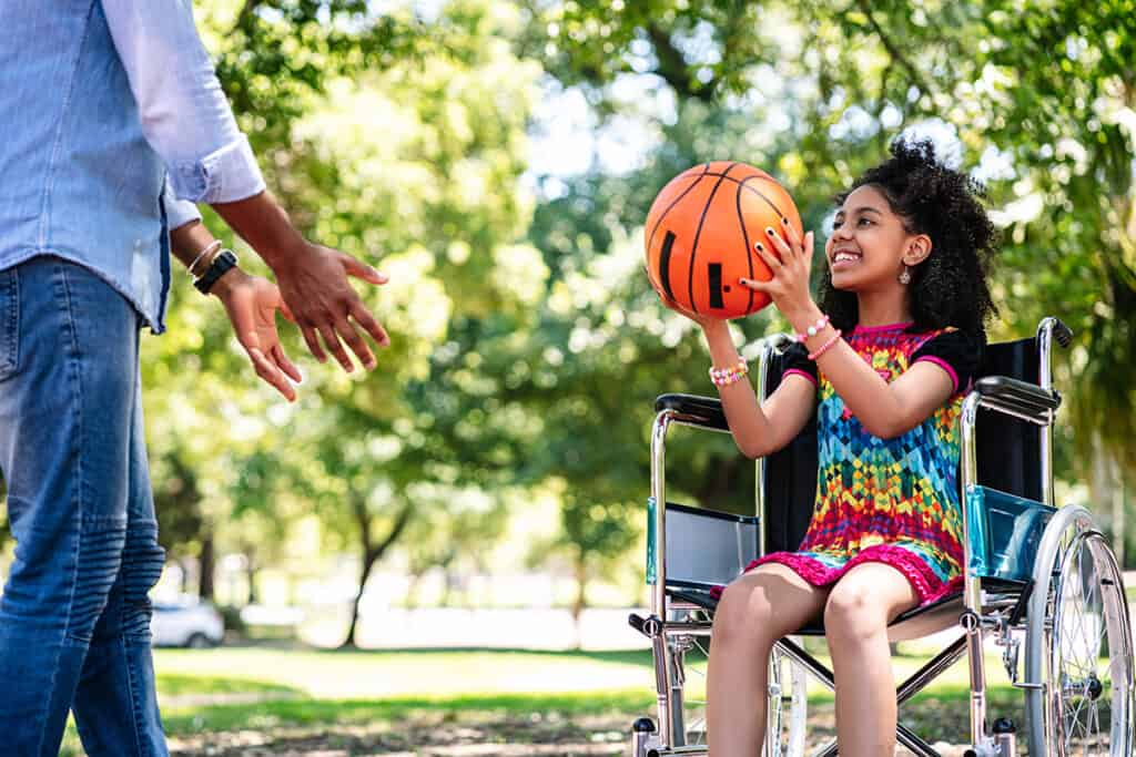 Little girl in a wheelchair playing basketball with her father.
