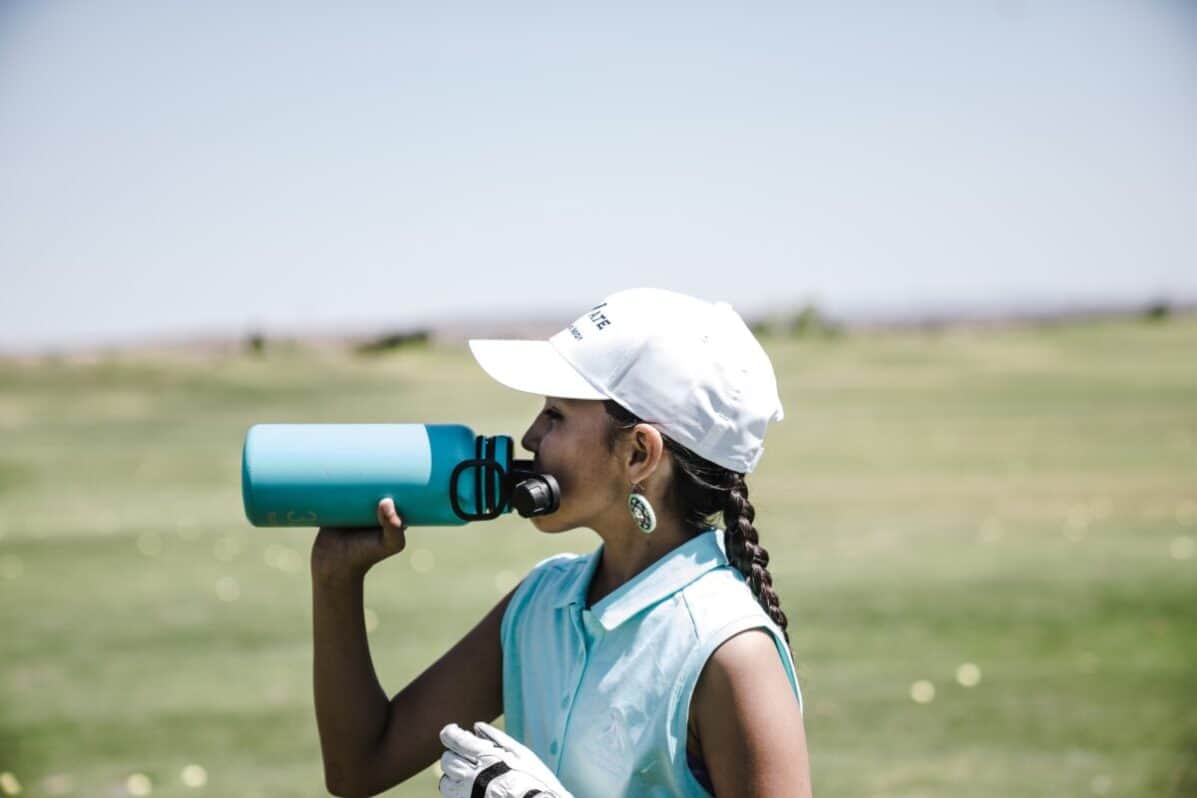 woman golfer drinking water out of a water bottle