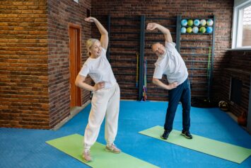 elderly woman and man on exercise mats stretching while standing
