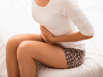 woman sitting while holding her stomach from gas and bloating pain from IBS